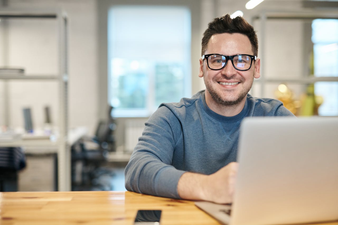 my-path Happy man wearing glasses working remotely on laptop in modern office environment.